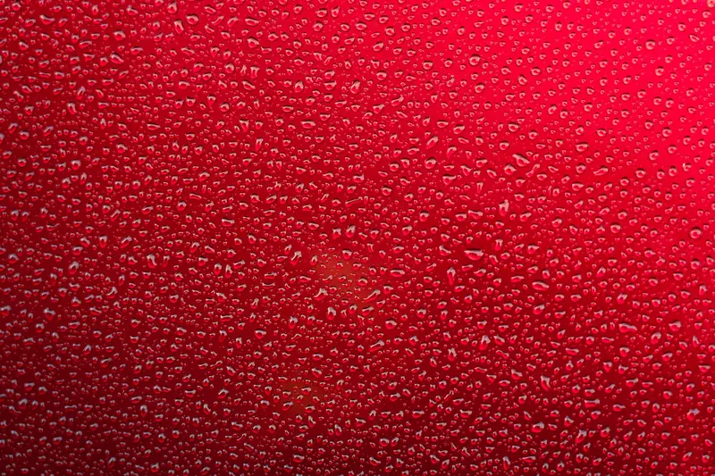 Close-up of tight water beads on glossy red paint