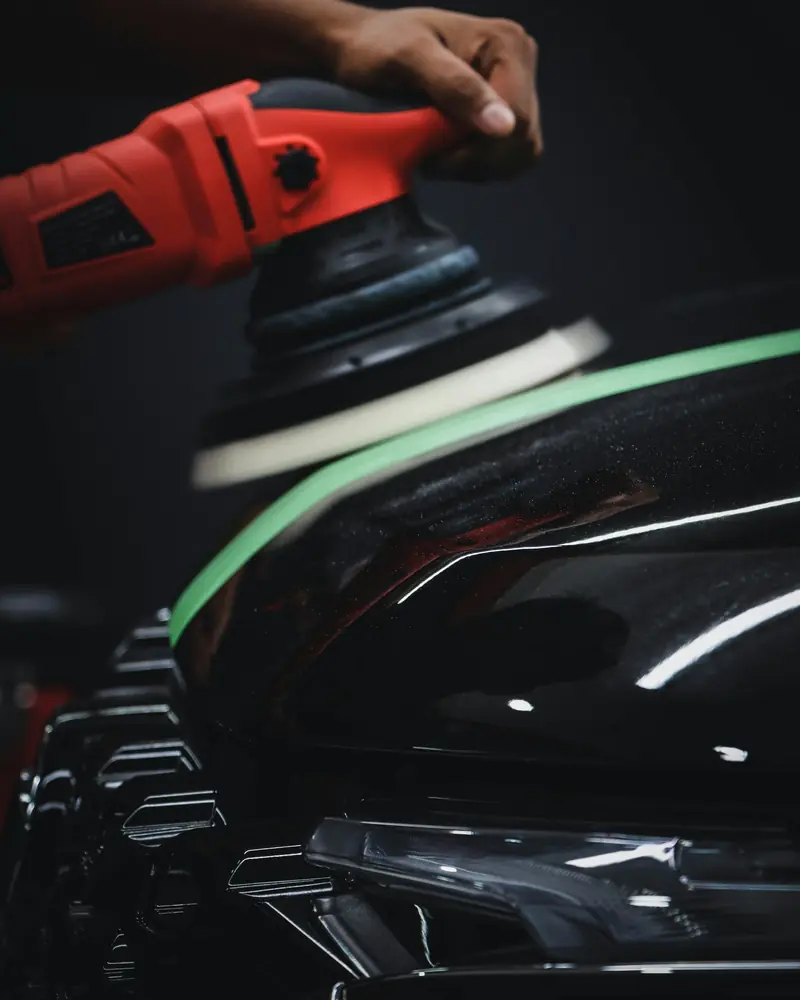A polisher on black paint with masking tape along the trim