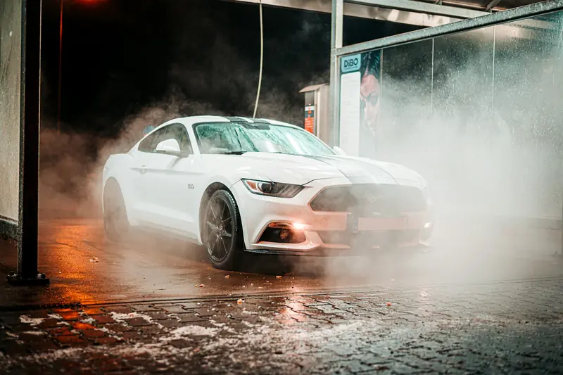 A white car covered in foam during a wash on a misty evening