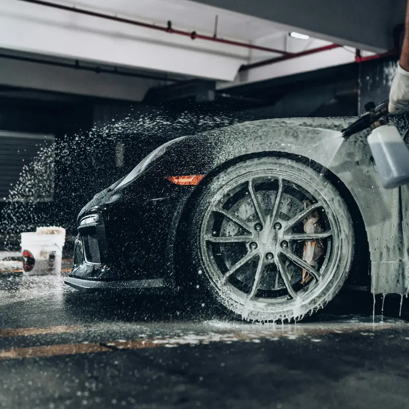 Snow foam rinsing off the wheel and wing of a black car